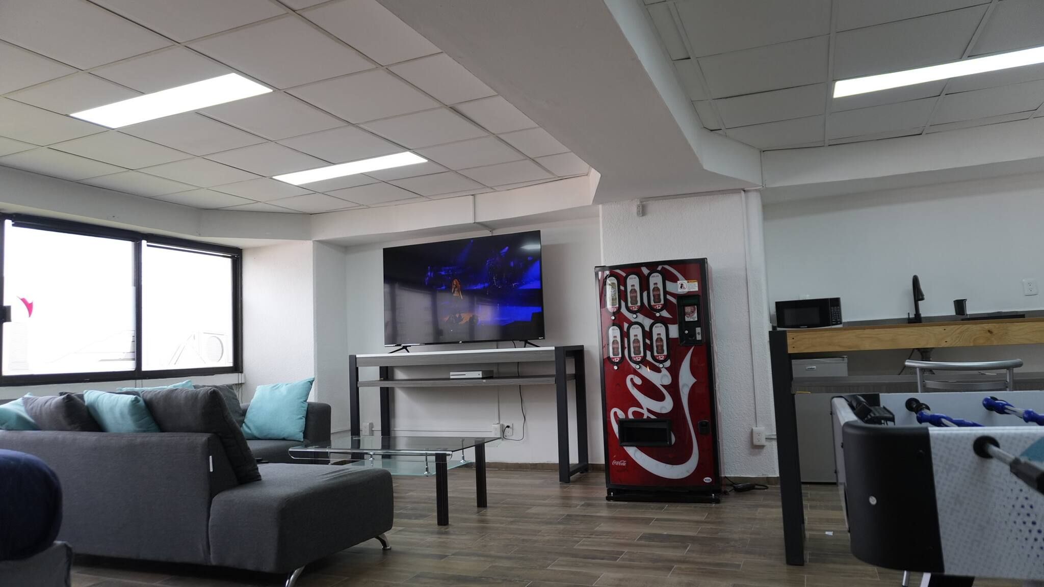 Een moderne kantoorruimte met een bank, een televisie, een automaat en een bureau met een computer.