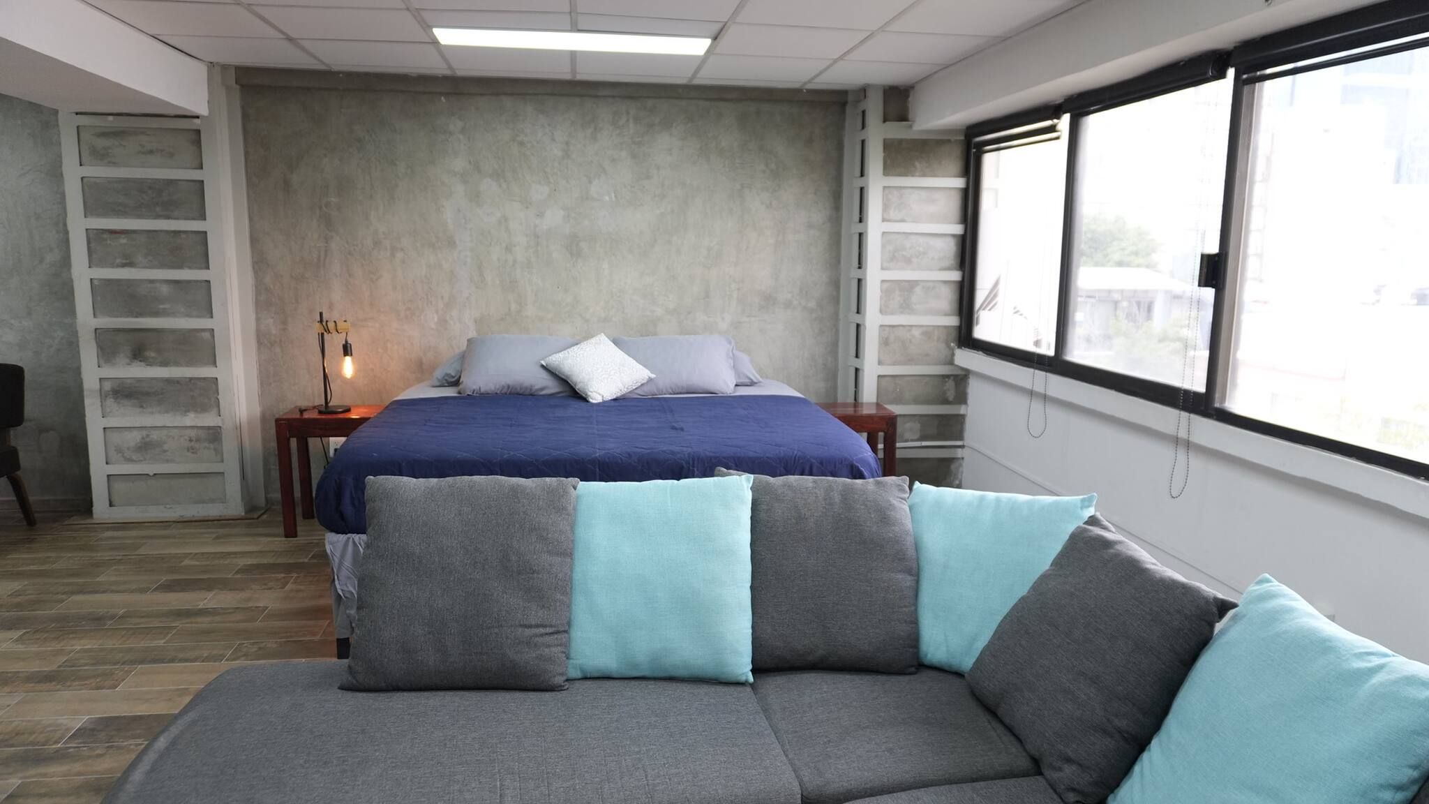 Un dormitorio con cama, sofá, mesita de noche y ventana.