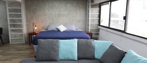 Un dormitorio con cama, sofá, mesita de noche y ventana.