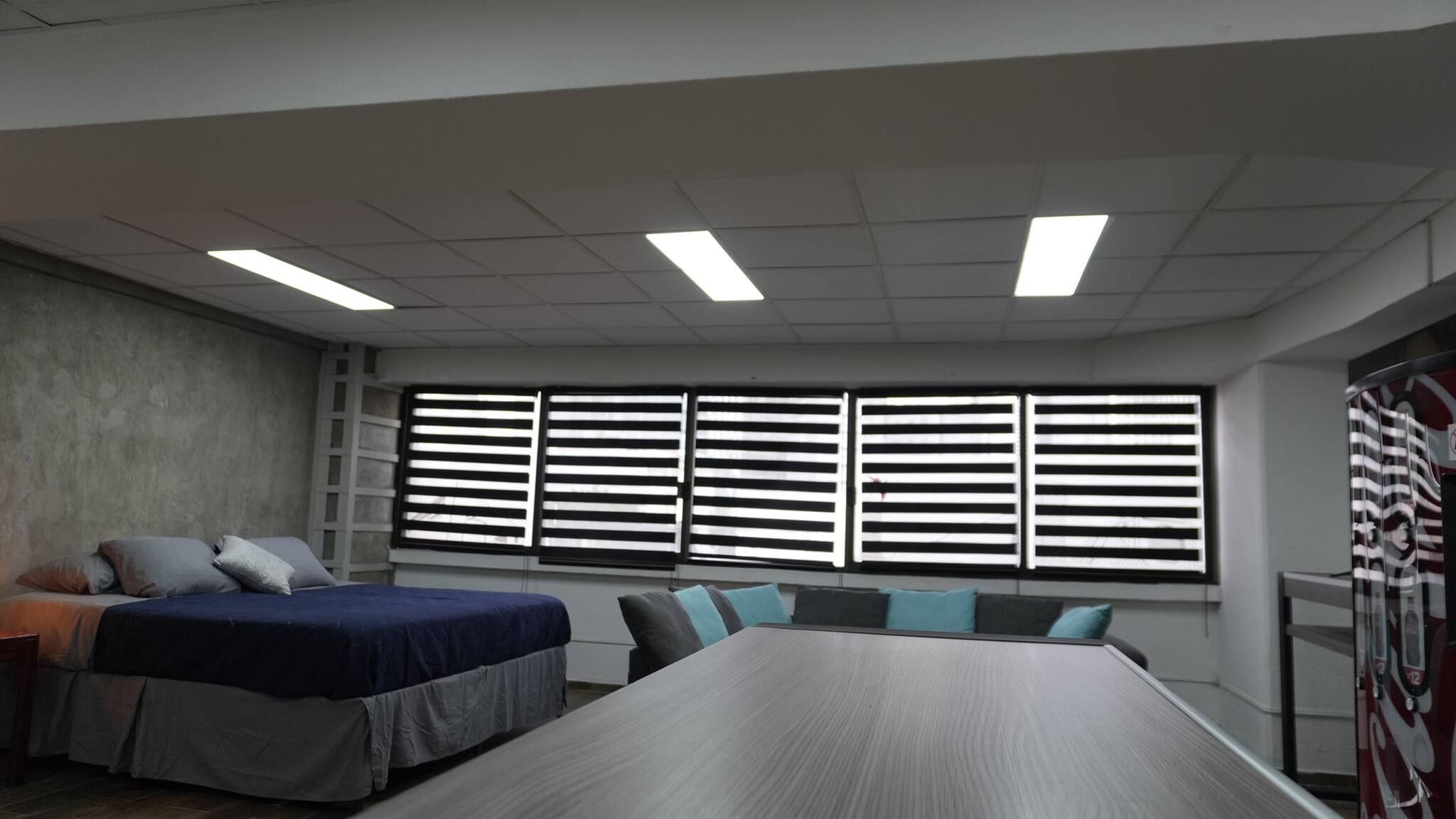 A conference room with a large table, a bed, and a window with blinds.