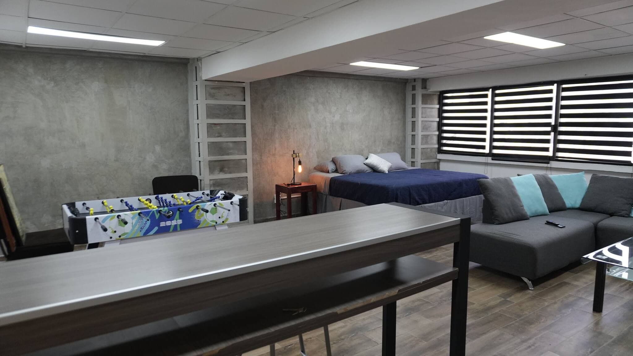 A modern room with a bed, a sofa, a desk, and a foosball table.