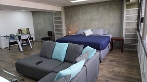 A modern hotel room with a sofa, a bed with blue bedding, a small table, and a foosball table. - Modern Loft King Bed, Wifi & Smart Lock (Mexico City)
