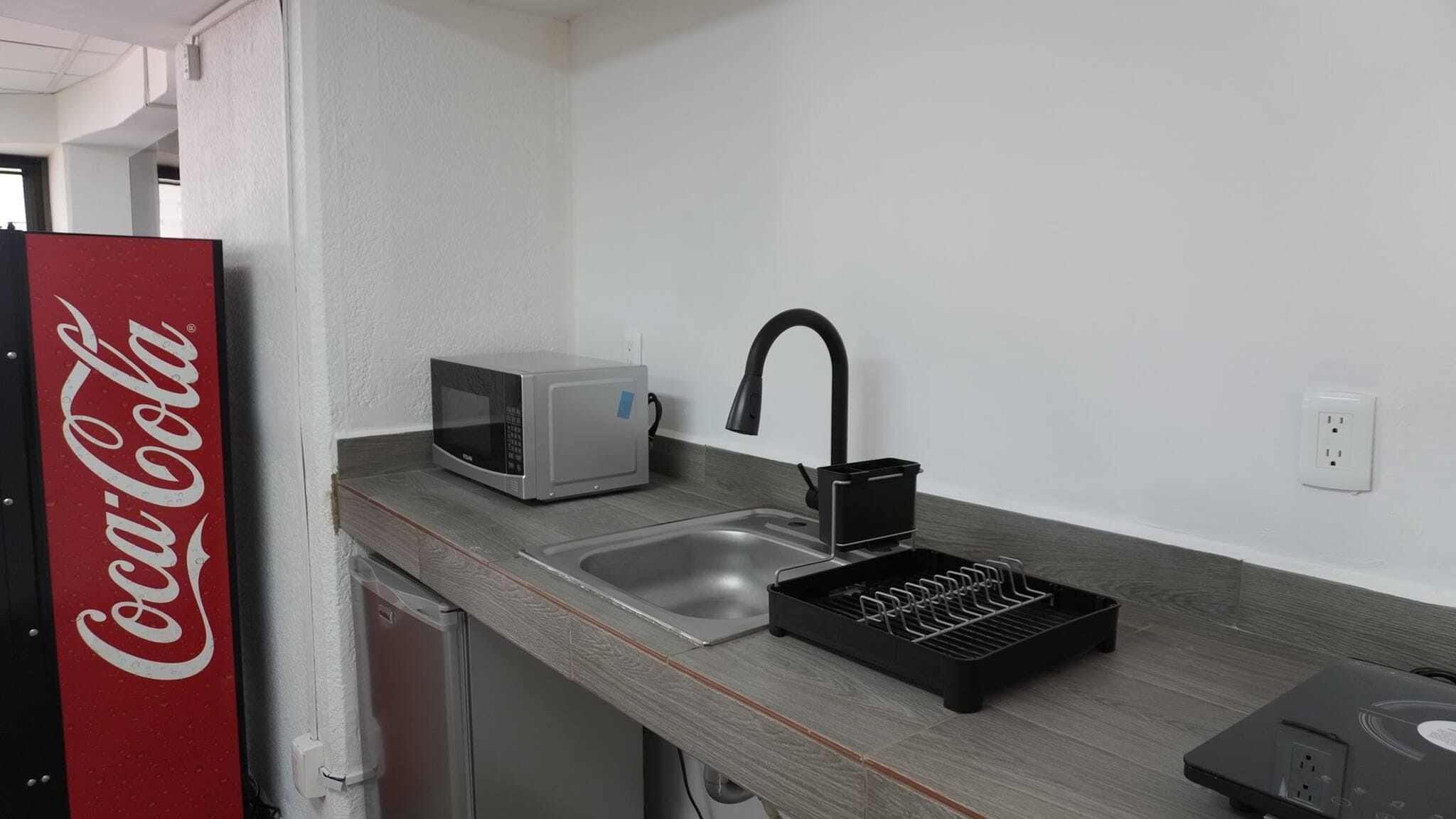 Een kitchenette met een magnetron, een spoelbak en een zwarte kraan.