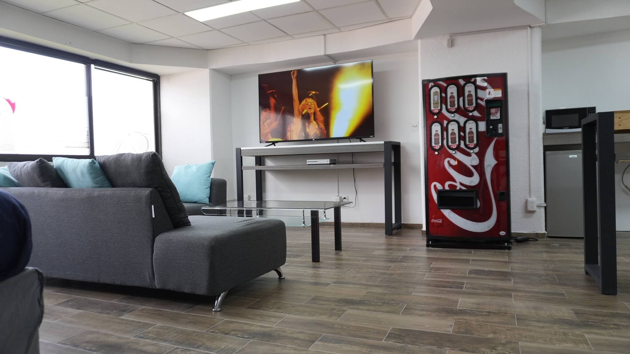 Un salon moderne avec un canapé, une table basse en verre, un téléviseur à écran plat et un distributeur automatique de Coca-Cola.