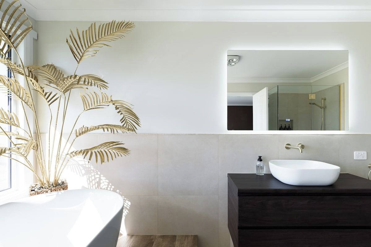 Een moderne badkamer met een witte wastafel, donkere badkamerkast en een grote spiegel.