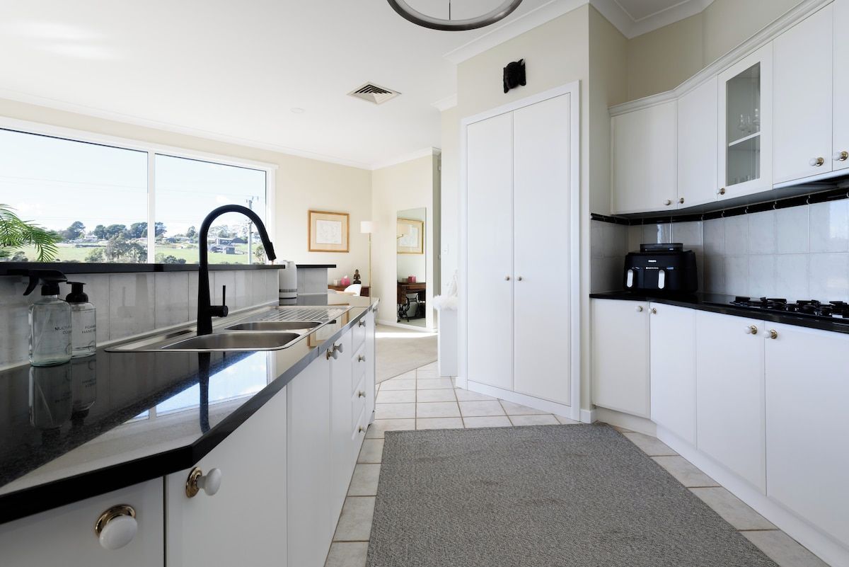 A modern kitchen with white cabinets, a black countertop, and a view of the outdoors.