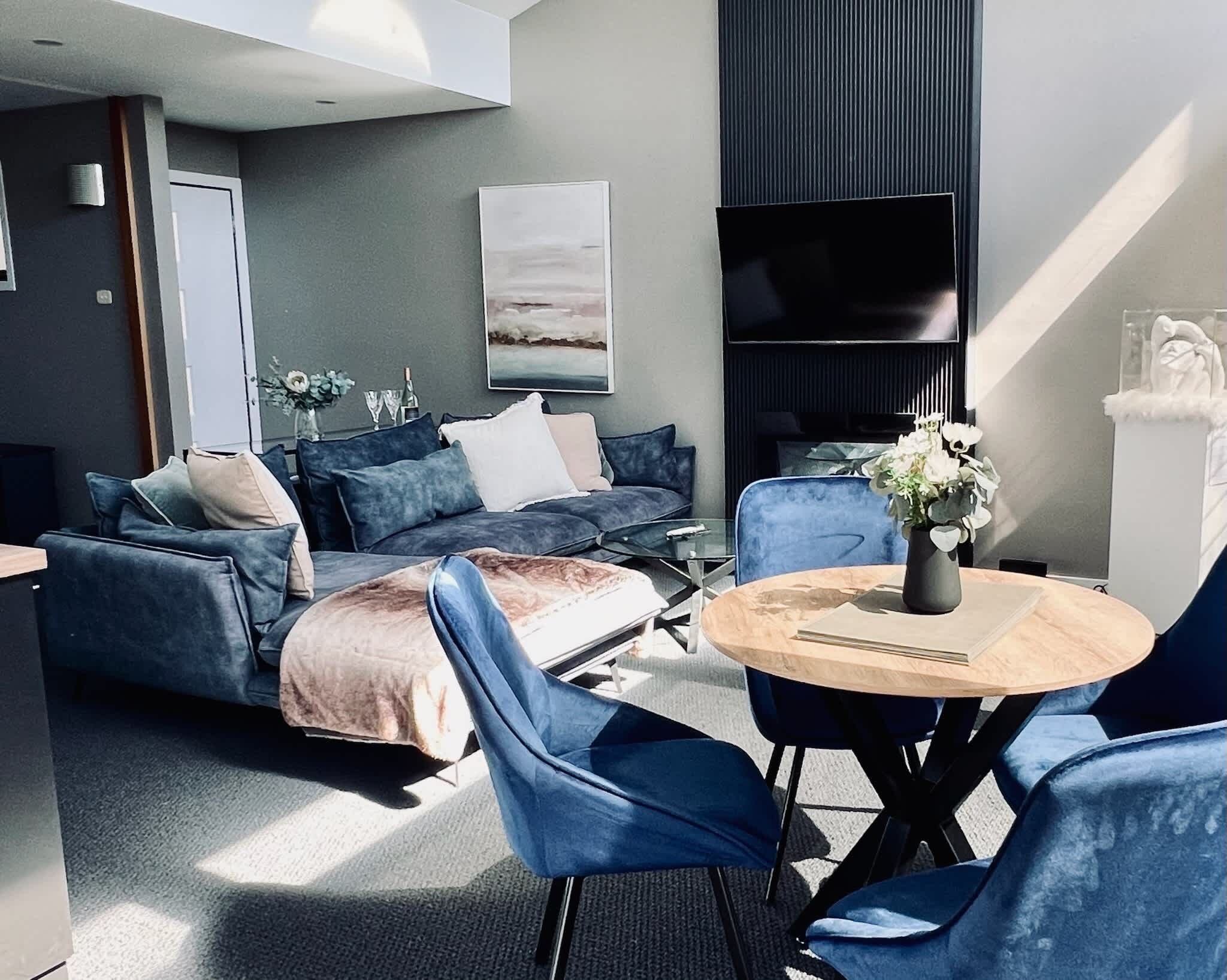 A modern living room with a sofa, chairs, a coffee table, and a flat-screen TV.