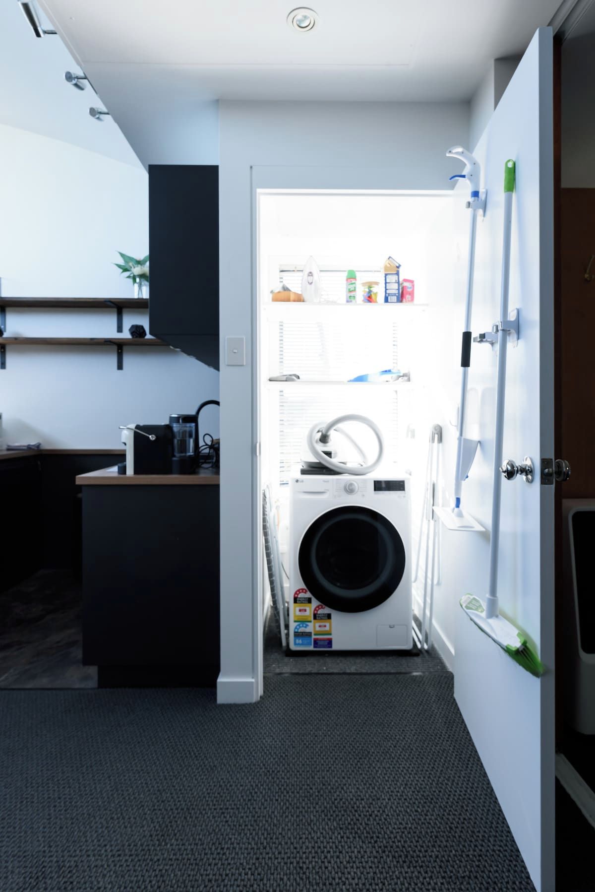Una sala de bugaderia amb una rentadora, una assecadora i una prestatgeria amb productes de neteja.