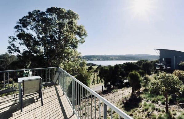 A deck with a table and chairs overlooking a landscape with trees and a distant view of hills.