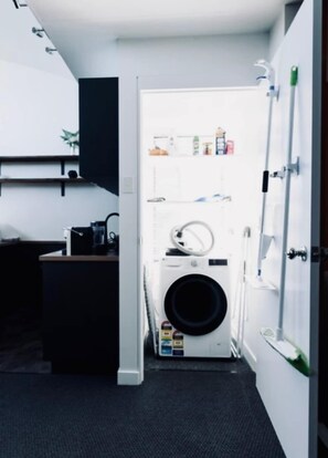 A compact laundry room with a washing machine, a drying rack, and a small shelf with toiletries.