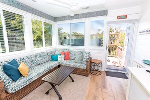 A sunlit room with a patterned sofa, a small table, and a view of the outdoors through large windows. - Oceanside- Private Pool, Hot Tub-SG113, Sandy Peach (Duck)