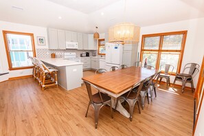 A modern kitchen with white cabinets, a central island, and a dining area with a wooden table and metal chairs. - Oceanside- Private Pool, Hot Tub-SG113, Sandy Peach (Duck)