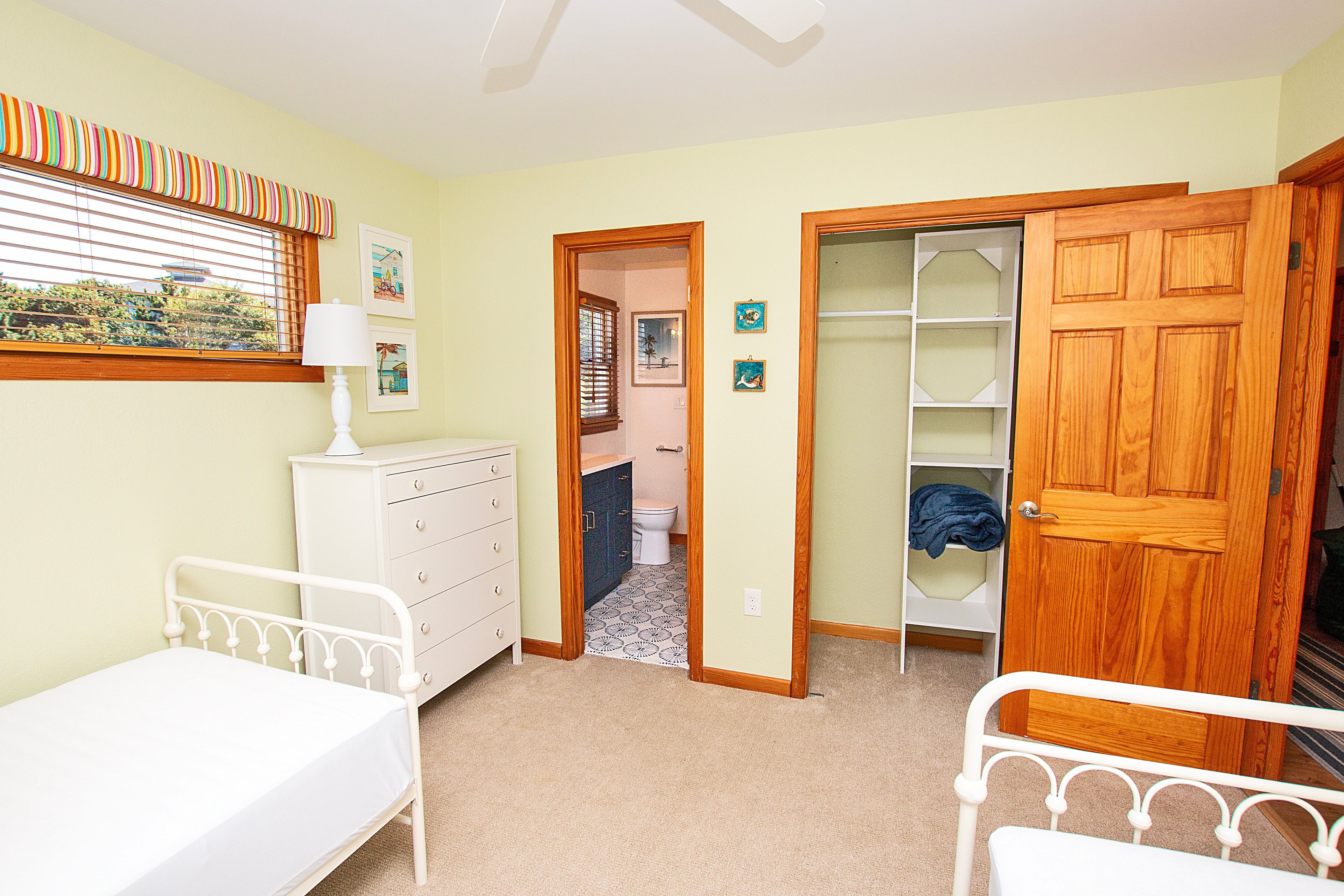 Een slaapkamer met een bed, een dressoir, een nachtkastje, een raam met jaloezieën en een deur naar een badkamer.