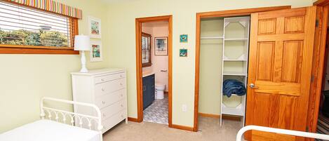 A bedroom with a bed, a dresser, a nightstand, a window with blinds, and a door leading to a bathroom.