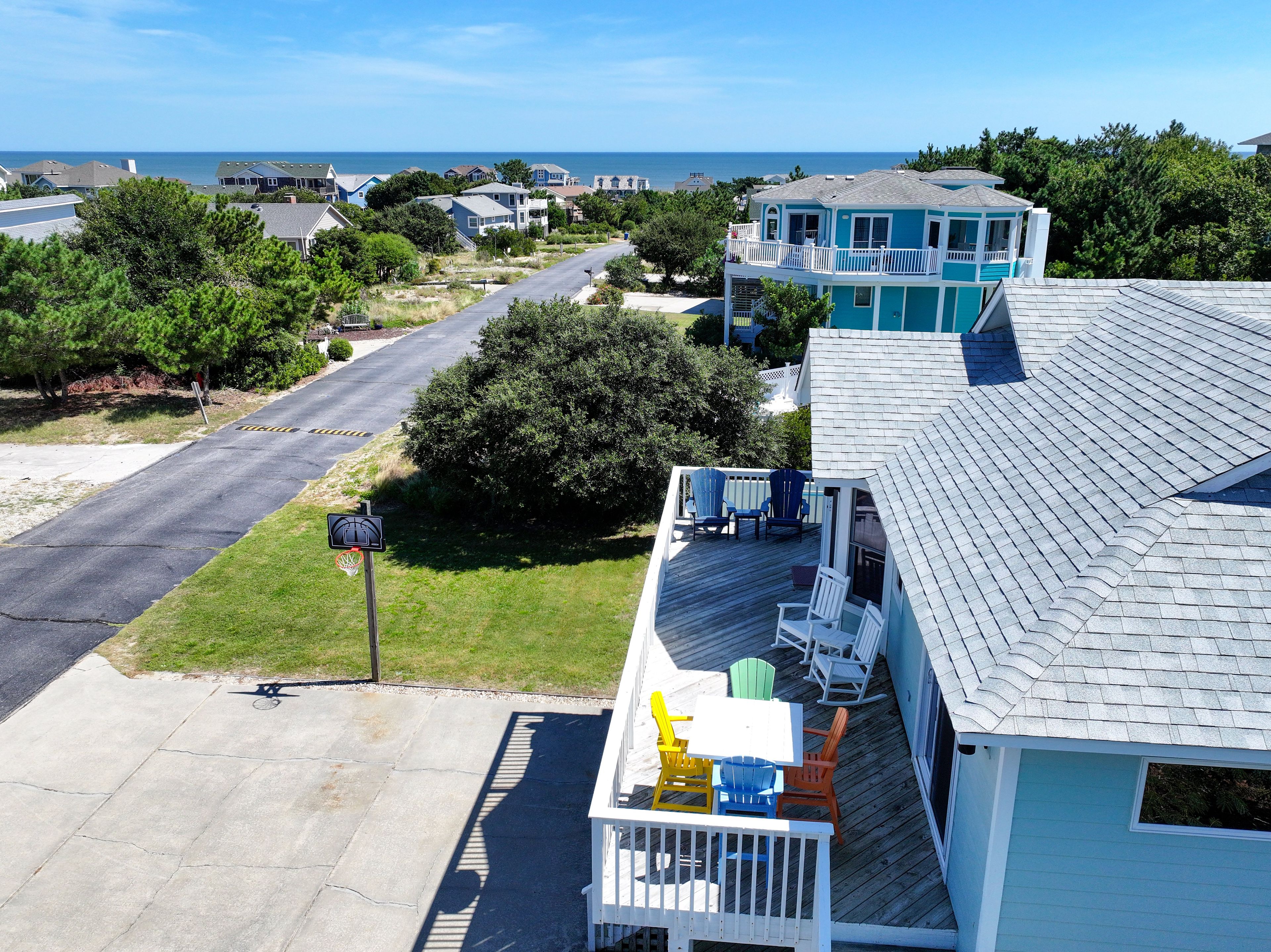 A residential area with a view of the ocean, a wooden deck with outdoor furniture, and a house with a blue exterior.
