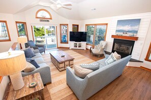 A spacious living room with a large television, comfortable seating, a fireplace, and large windows offering views of the outdoors. - Oceanside- Private Pool, Hot Tub-SG113, Sandy Peach (Duck)