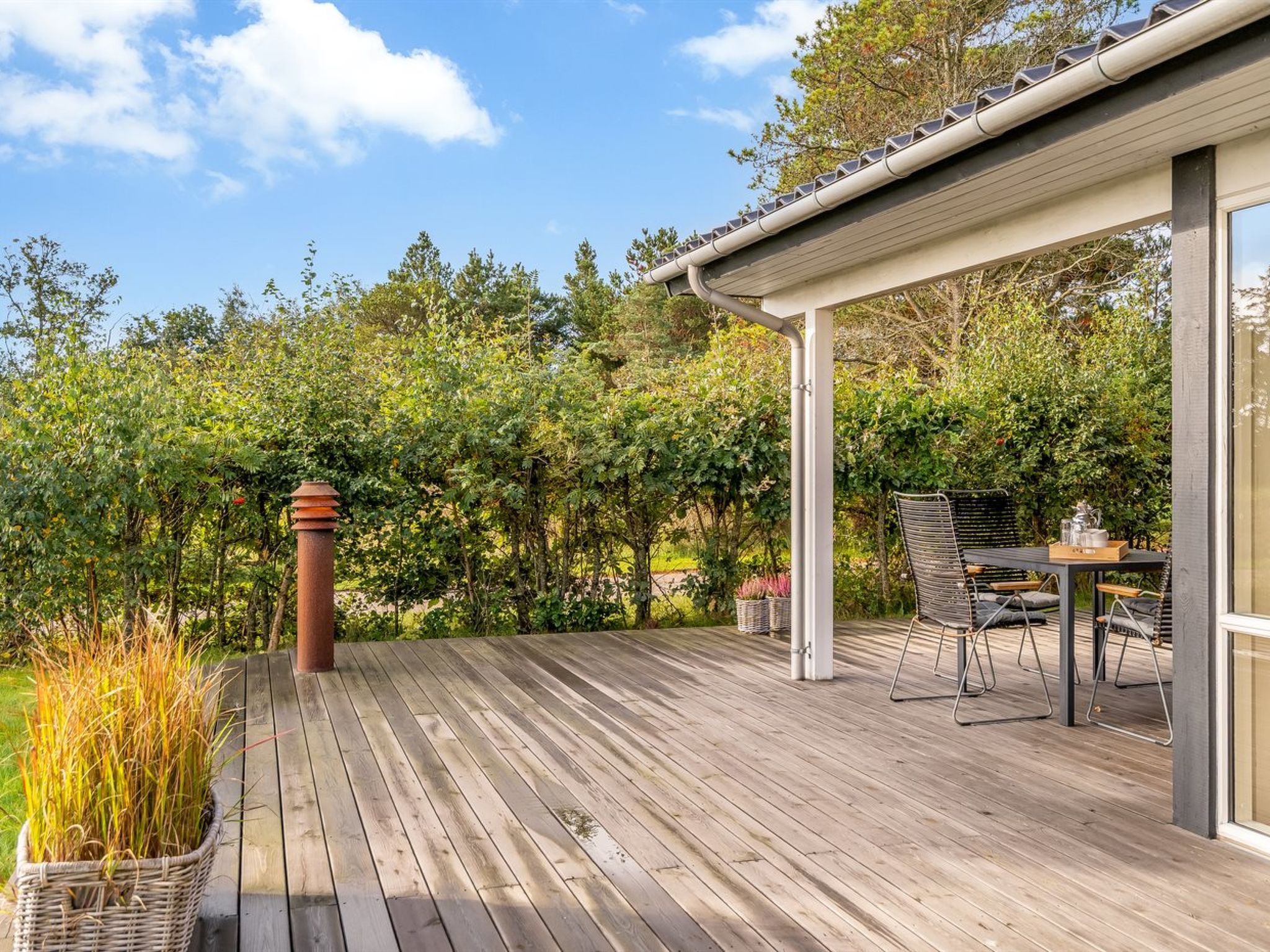 A wooden deck with a pergola, outdoor furniture, and a view of a lush garden.