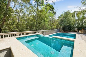 A swimming pool with a wooden deck and a stone border, surrounded by trees. - 🐚 Gone Coastal | Private Heated Pool + Hot Tub | Bikes | Fire Pit (Santa Rosa Beach)