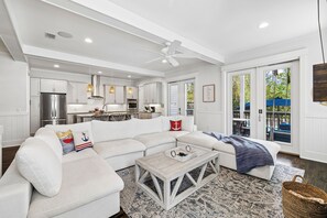 A spacious living room with a white sofa, a coffee table, and a view of the kitchen and outdoor area. - 🐚 Gone Coastal | Private Heated Pool + Hot Tub | Bikes | Fire Pit (Santa Rosa Beach)