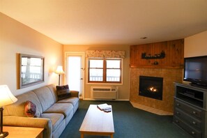 A living room with a sofa, a coffee table, a fireplace, a television, and a window with a view. - Deer Park 2 Bedroom with near Loon Mountain! (Woodstock)