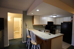 A kitchen with a bar area, white cabinets, a black refrigerator, and a wooden countertop. - Deer Park 2 Bedroom with near Loon Mountain! (Woodstock)
