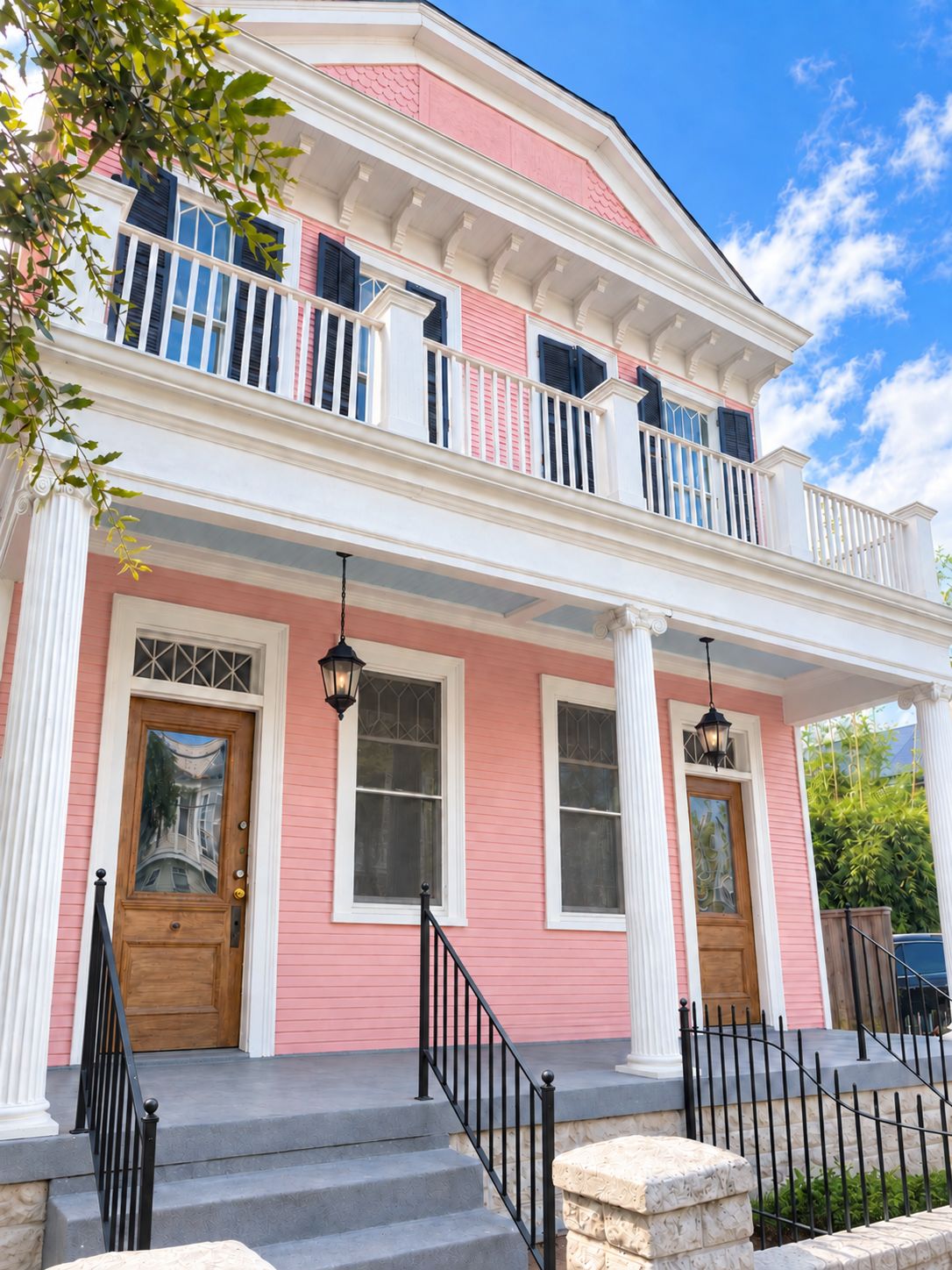 Une maison à deux étages avec une façade rose, des ornements blancs et un balcon doté de balustrades noires.