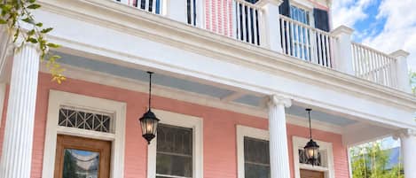 Une maison à deux étages avec une façade rose, des ornements blancs et un balcon doté de balustrades noires.