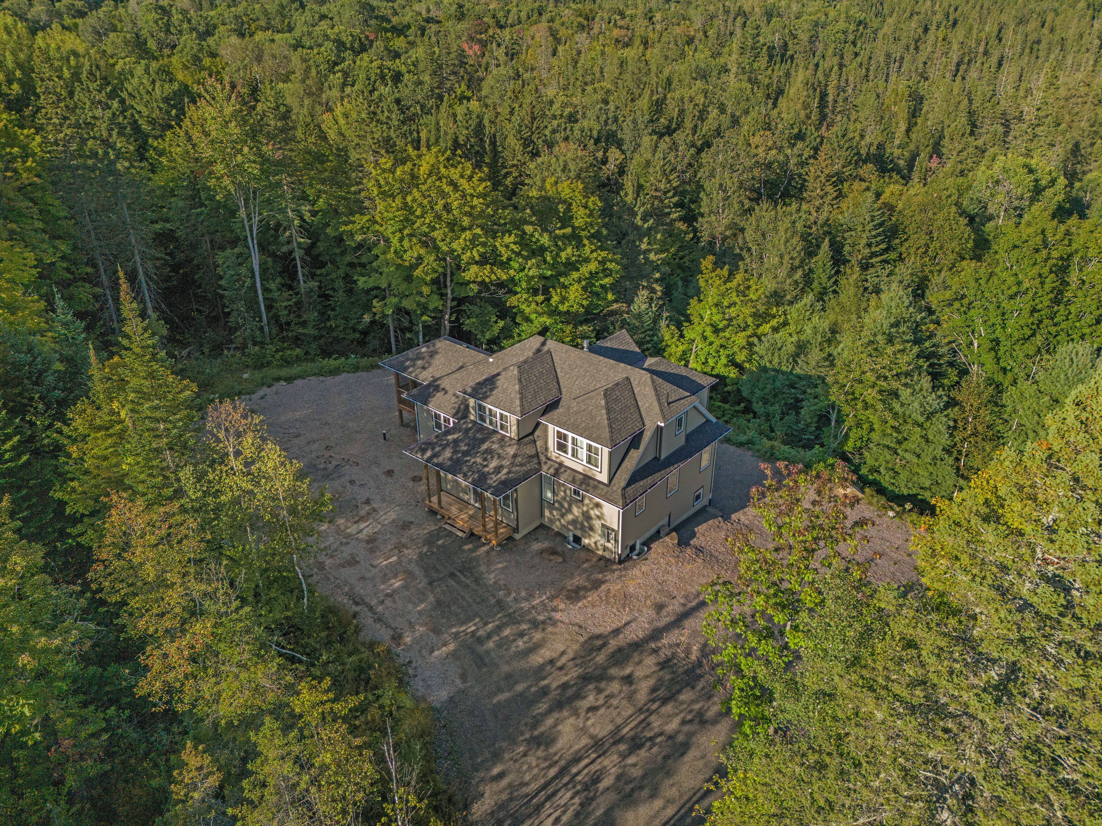 Une maison à deux étages, dotée d’une grande allée et entourée d’une forêt dense.