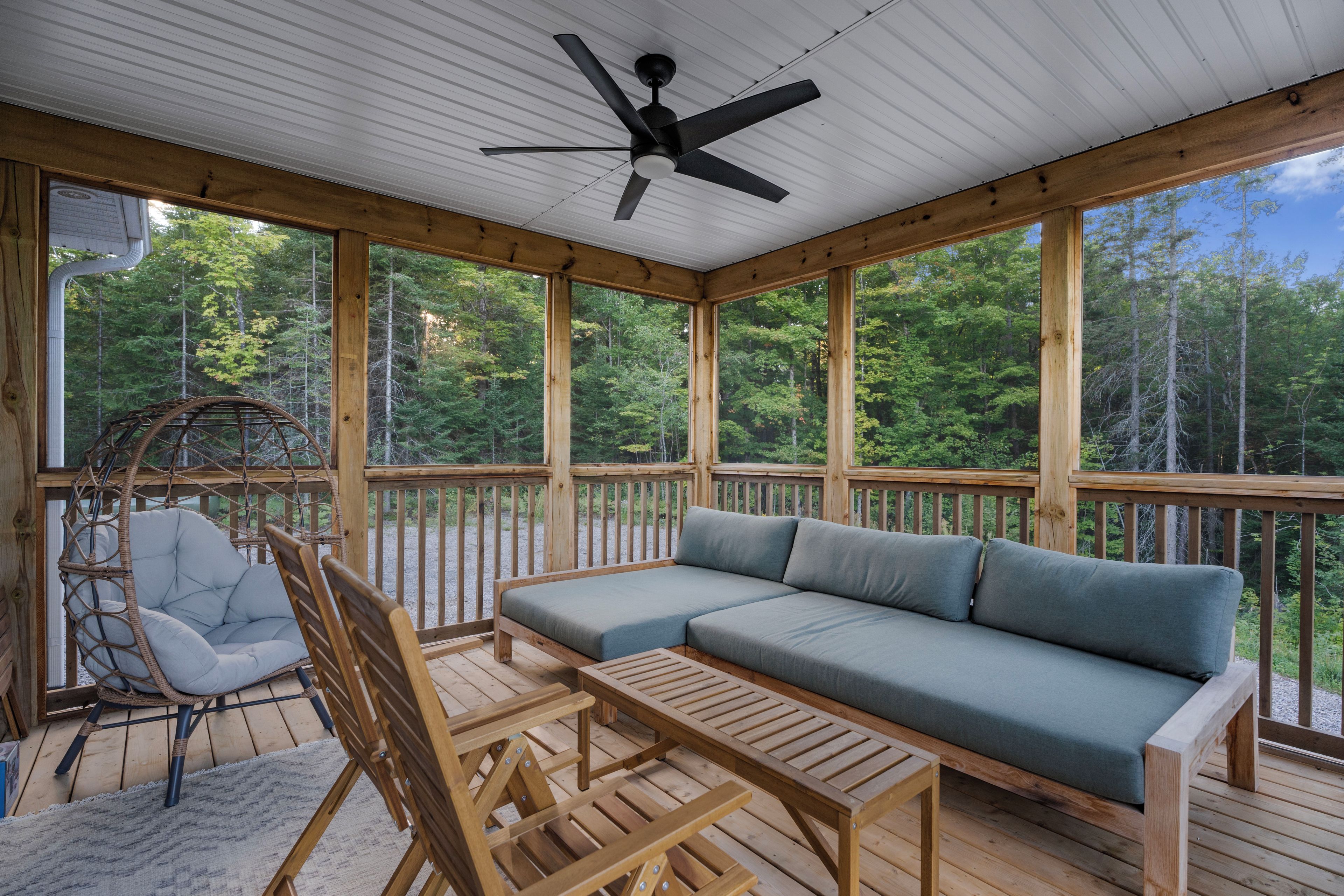 Une terrasse couverte, aménagée avec un canapé, des fauteuils et une table, qui offre une vue sur une forêt.