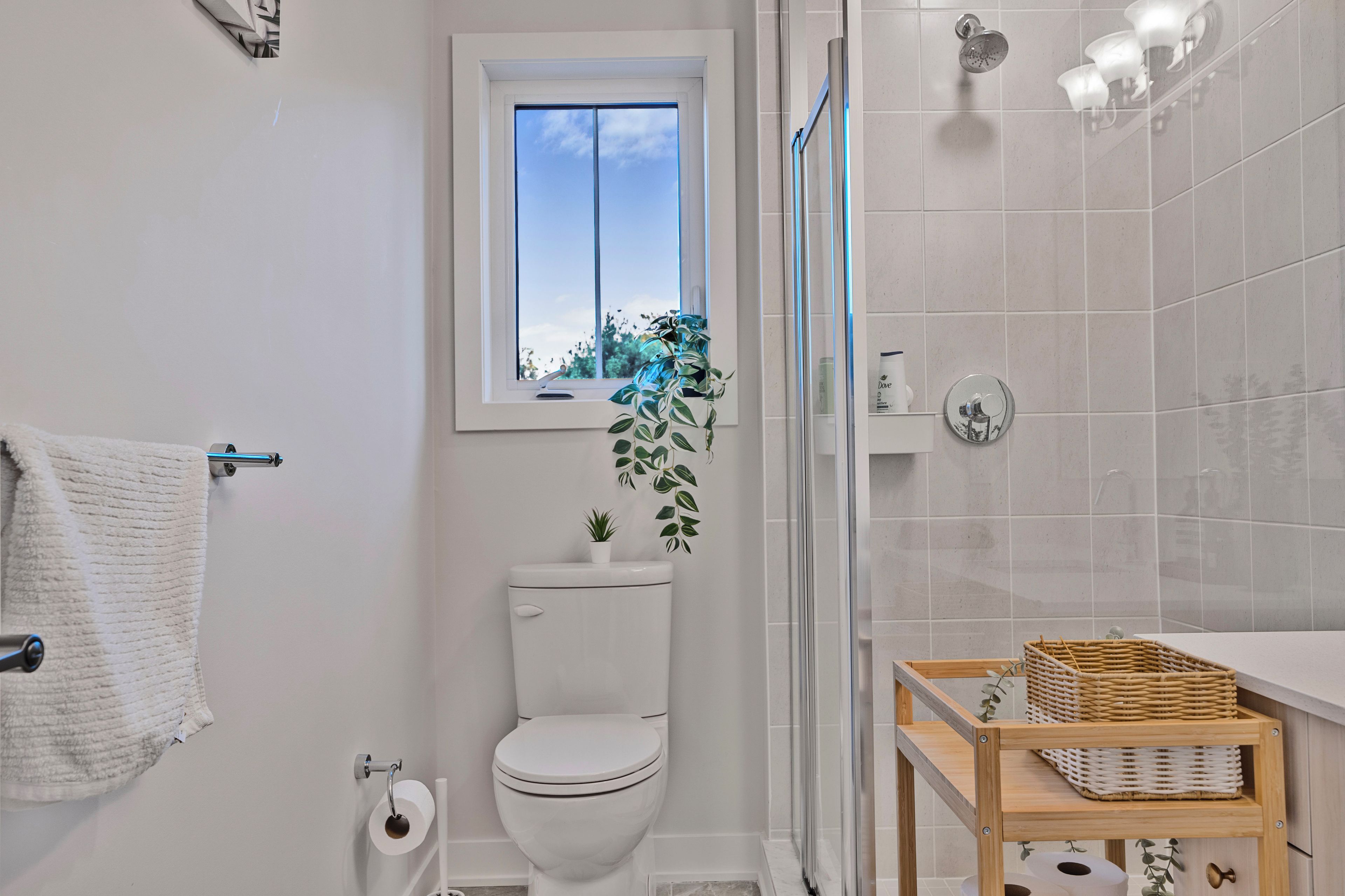 Un baño con inodoro, ventana, ducha y repisa de madera con cestas.