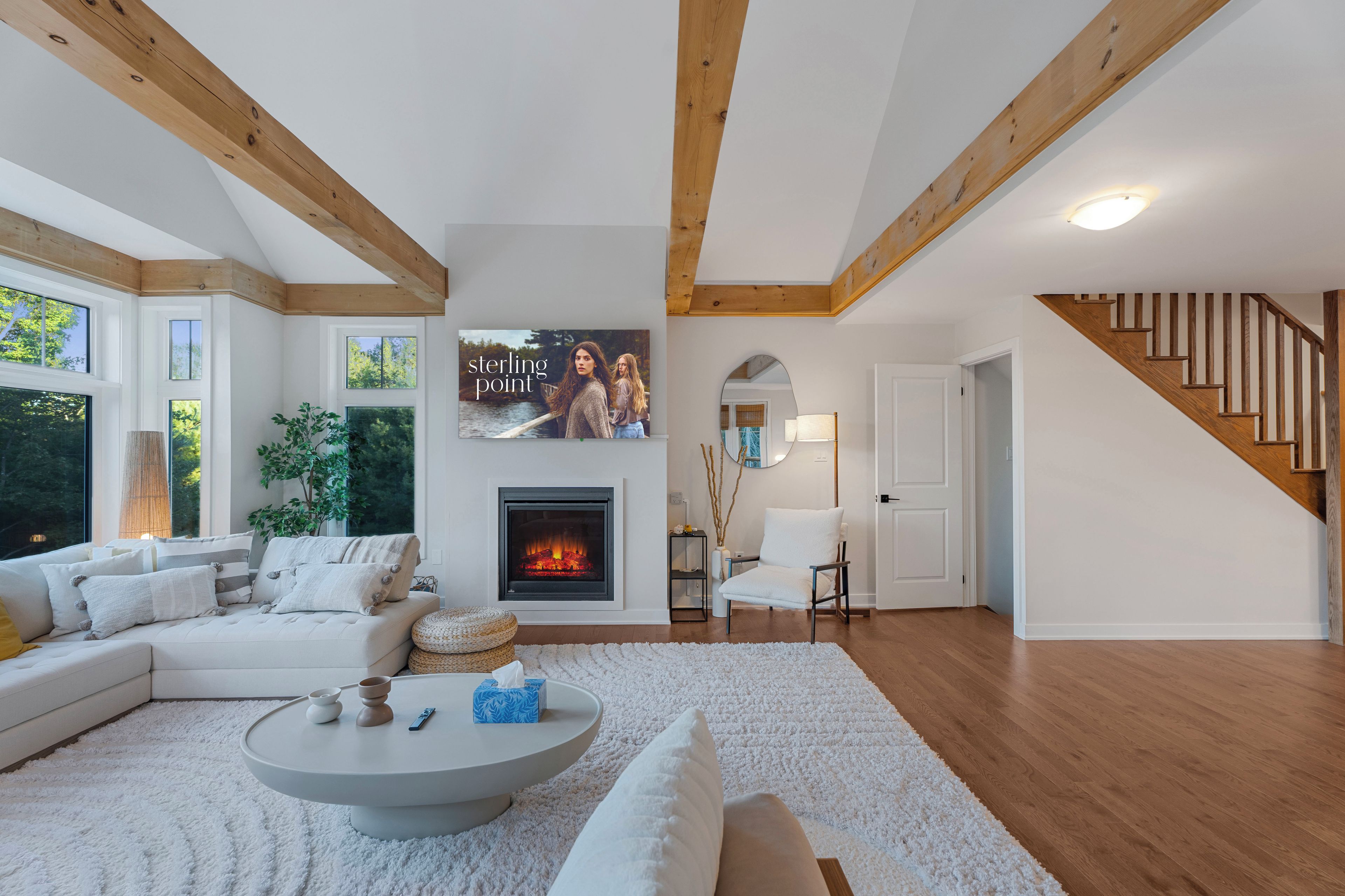 Una sala de estar moderna con chimenea, vigas de madera, una escalera y un ventanal grande.