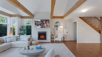Ein modernes Wohnzimmer mit Kamin, Holzbalken, einer Treppe und einem großen Fenster.