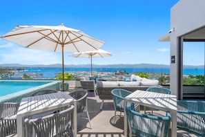 Eine Terrasse mit Sitzgelegenheiten im Freien, einem Schwimmbad und Blick auf den Hafen und das Meer.