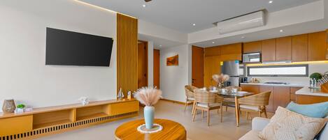 Una sala moderna con un televisor de pantalla plana, un comedor con mesa y sillas, y una cocina con microondas y refrigerador.