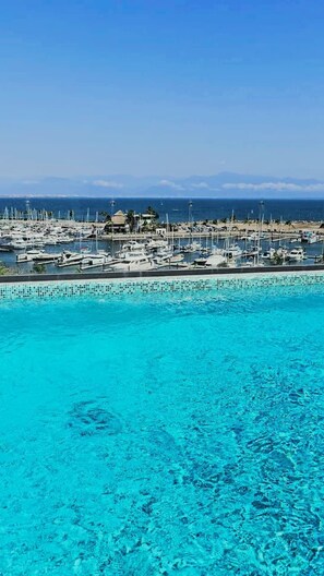 Ein Yachthafen mit vertäuten Booten, ein klares blaues Schwimmbecken und Blick auf den Ozean.