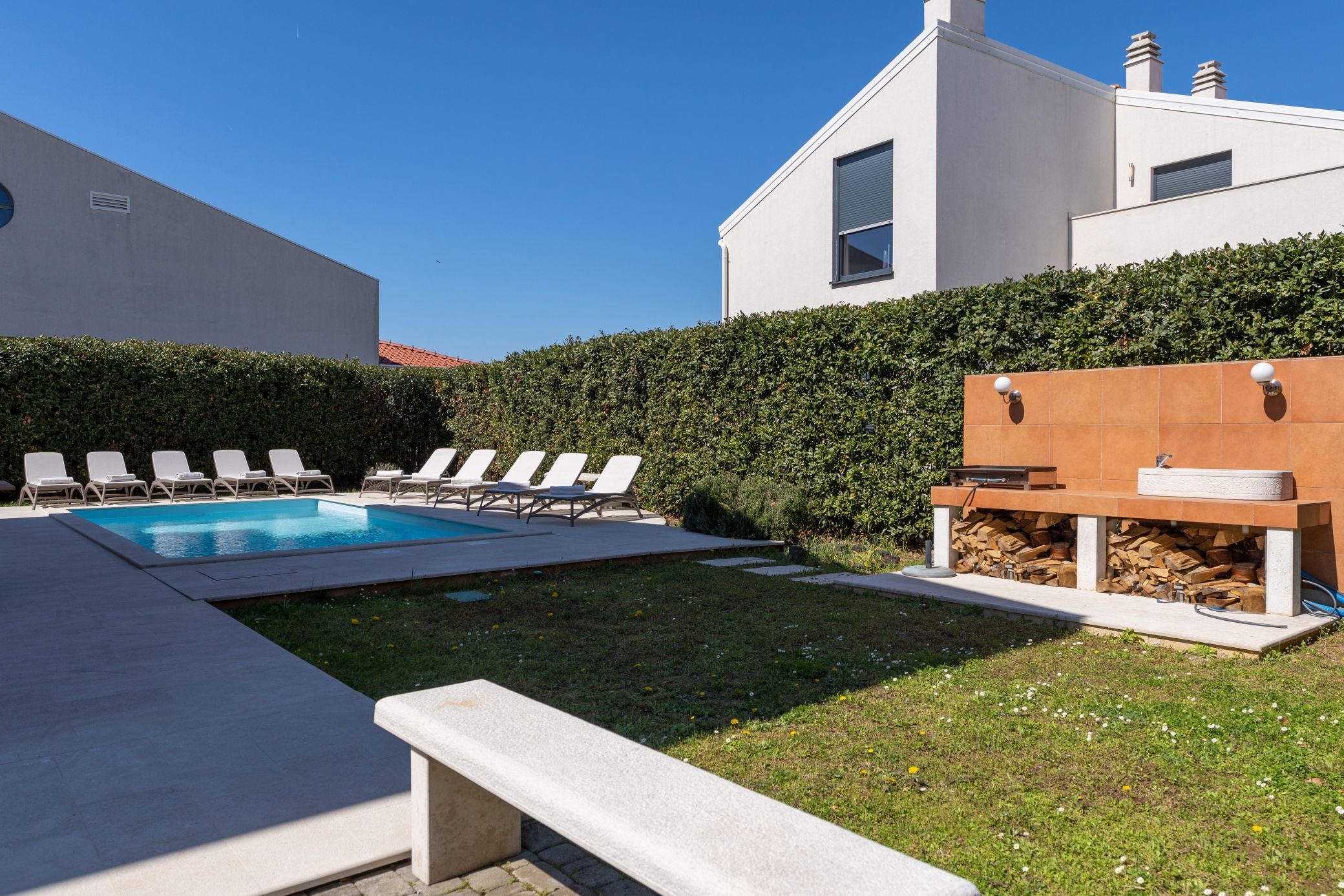 Ein moderner Poolbereich im Freien mit Liegestühlen, einer Holzterrasse und einer Steinsitzbank.