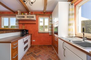 A compact kitchen with a tiled floor, wooden cabinets, a built-in oven, and a window with curtains. - Villa Leon (Istria - Funtana) (Funtana)
