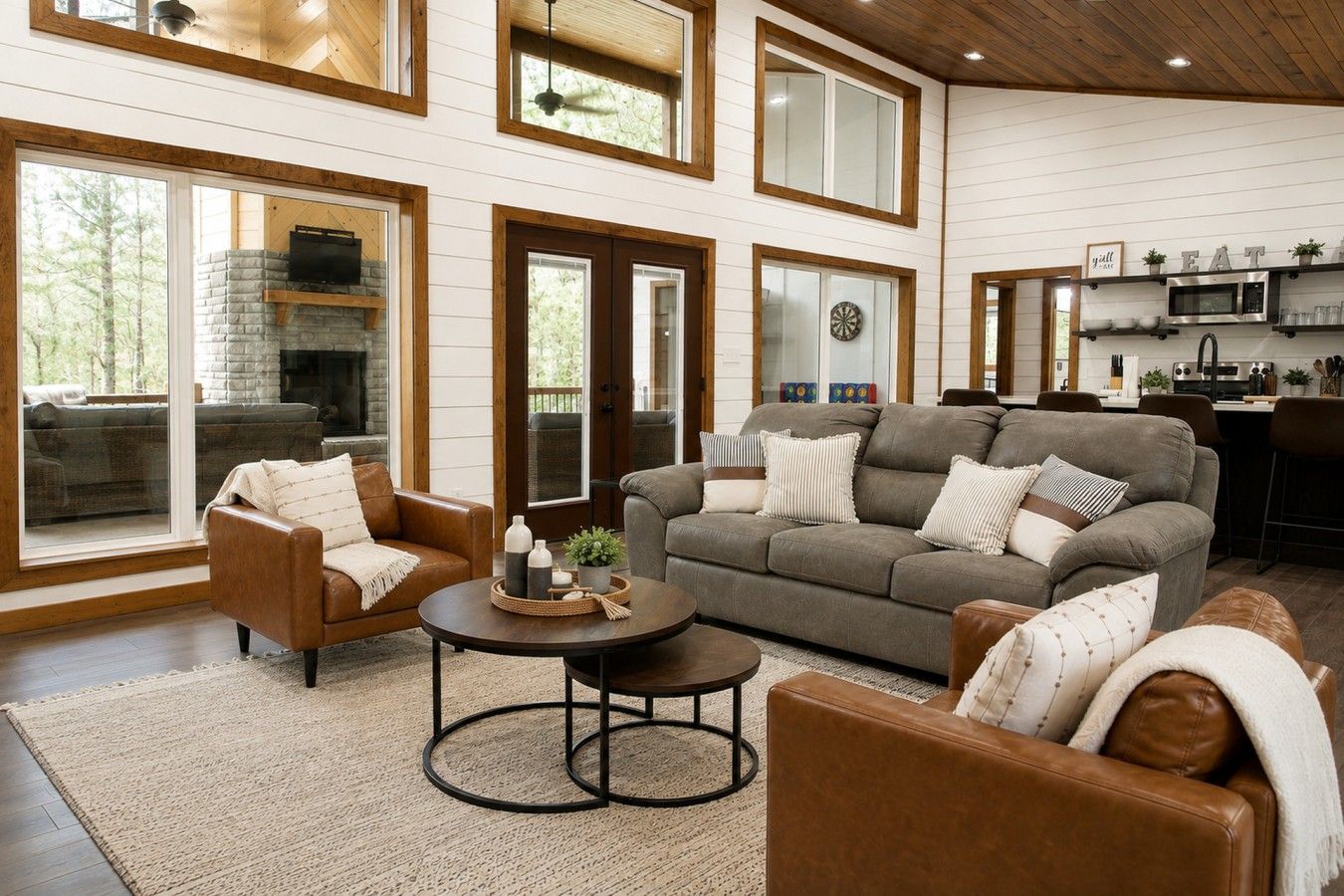 Amplia sala de estar con chimenea, comedor con cocina al fondo y ventanas grandes.