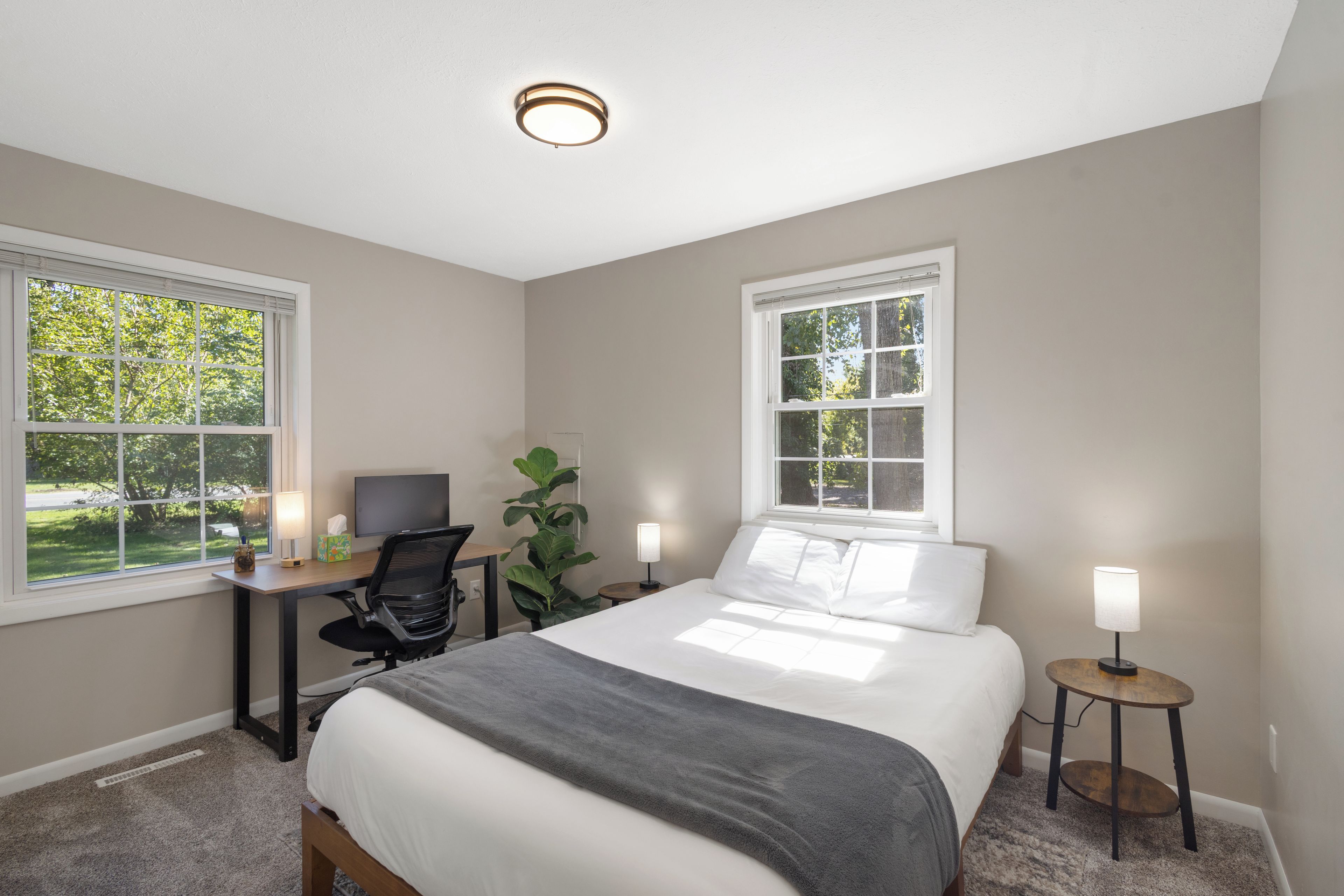 A bedroom with a bed, desk, chair, and two bedside lamps.