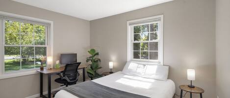 A bedroom with a bed, desk, chair, and two bedside lamps.