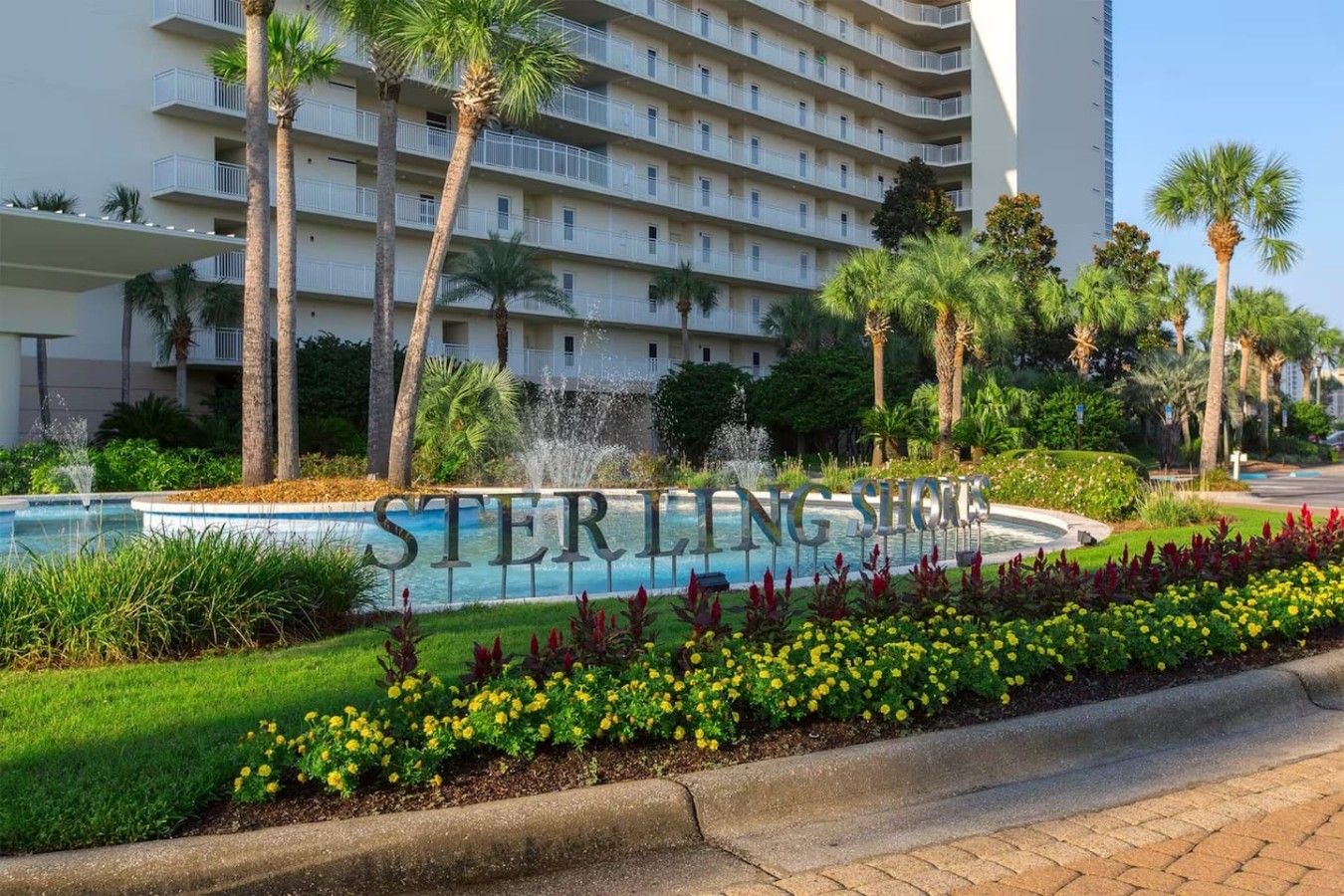 Een hotel met een zwembad, palmbomen en een bord met de tekst 'STERLING SHORES'.