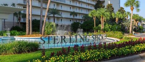 Een hotel met een zwembad, palmbomen en een bord met de tekst 'STERLING SHORES'.