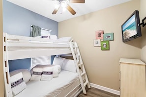 A bunk bed room with a ceiling fan, a small desk, and a wall-mounted TV. - Gulf View Condo | Pool | Sleeps 6 (Destin)