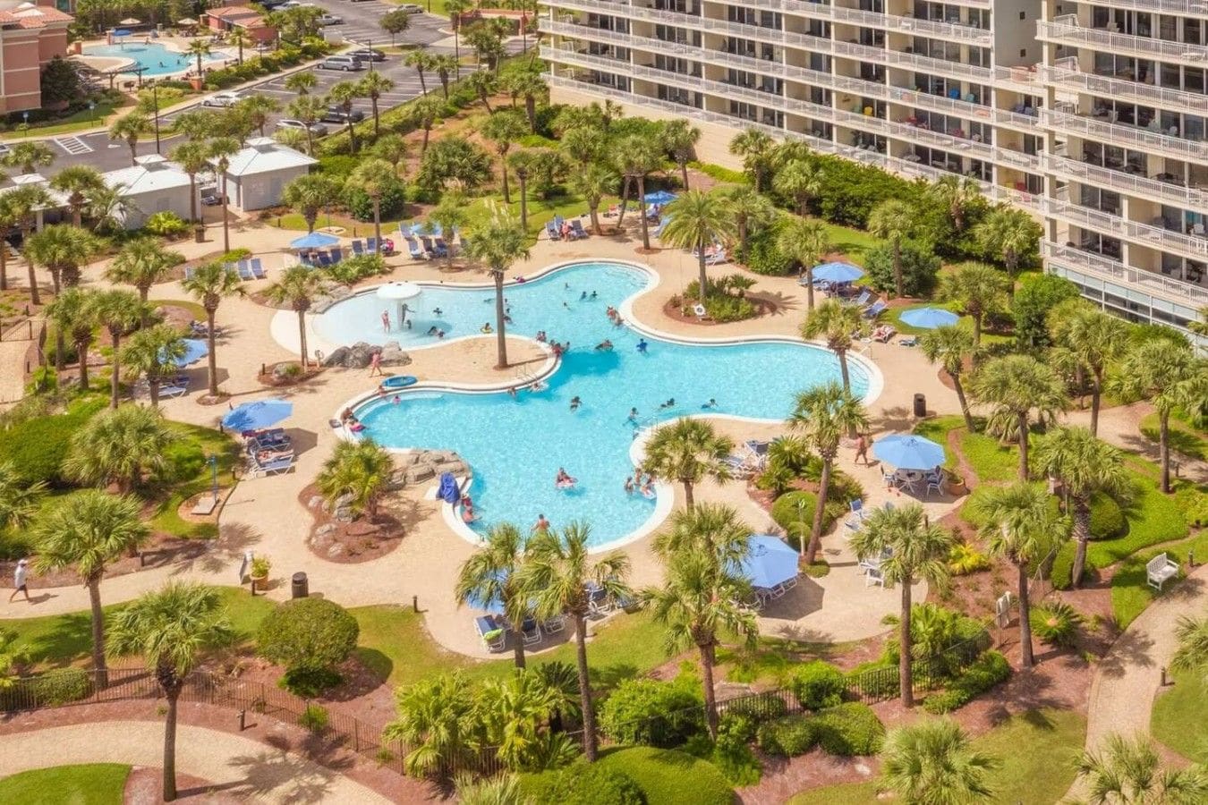 Um resort com várias piscinas, palmeiras e um edifício grande com varandas.