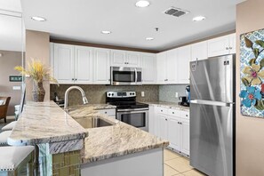 A modern kitchen with white cabinets, stainless steel appliances, and a marble countertop. - Gulf View Condo | Pool | Sleeps 6 (Destin)