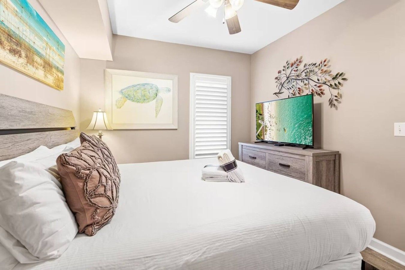Un dormitorio con cama, televisión, ventilador de techo y obras de arte en las paredes.