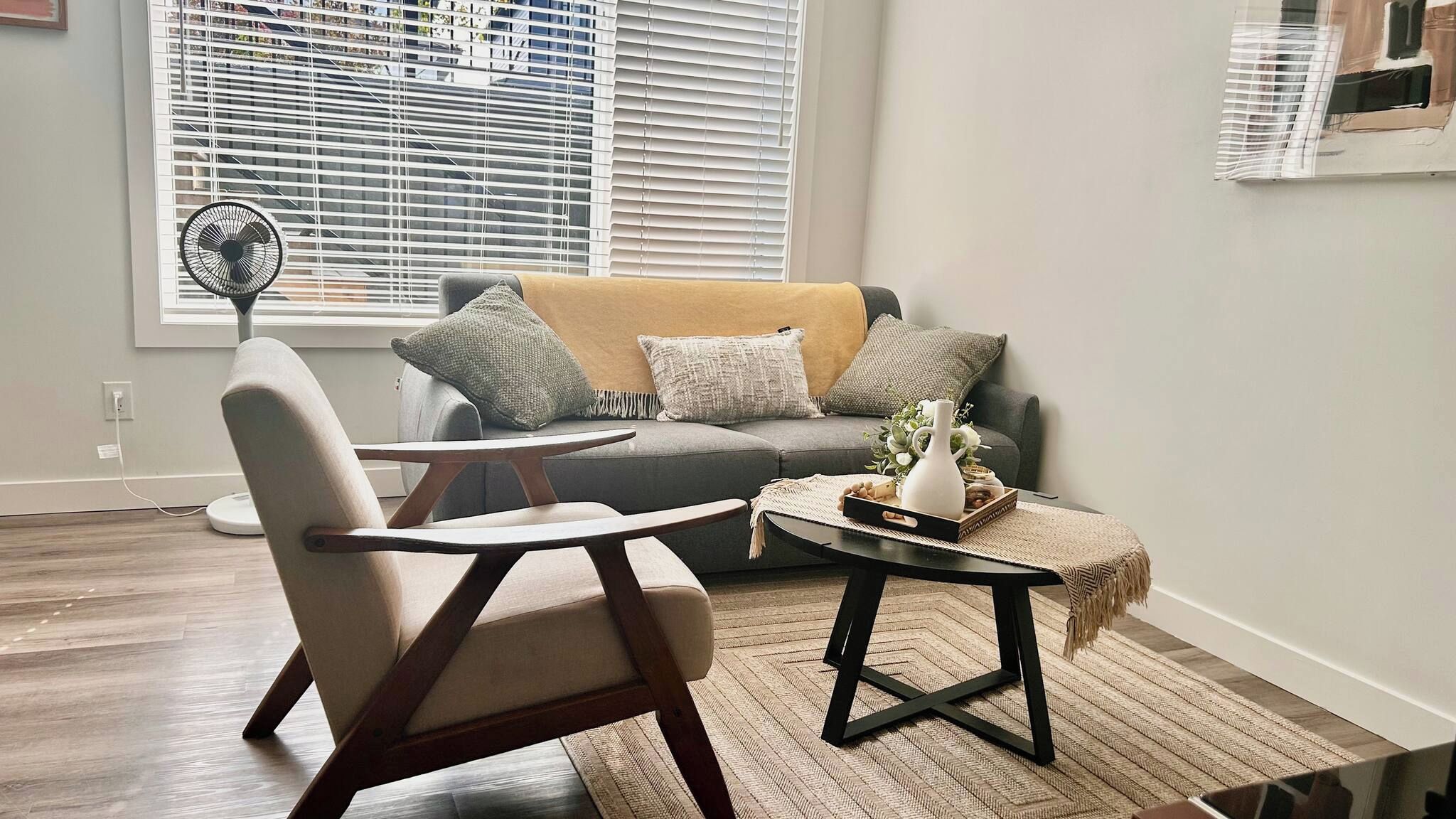A modern living room with a grey sofa, a wooden chair, a small round table, and a floor lamp.