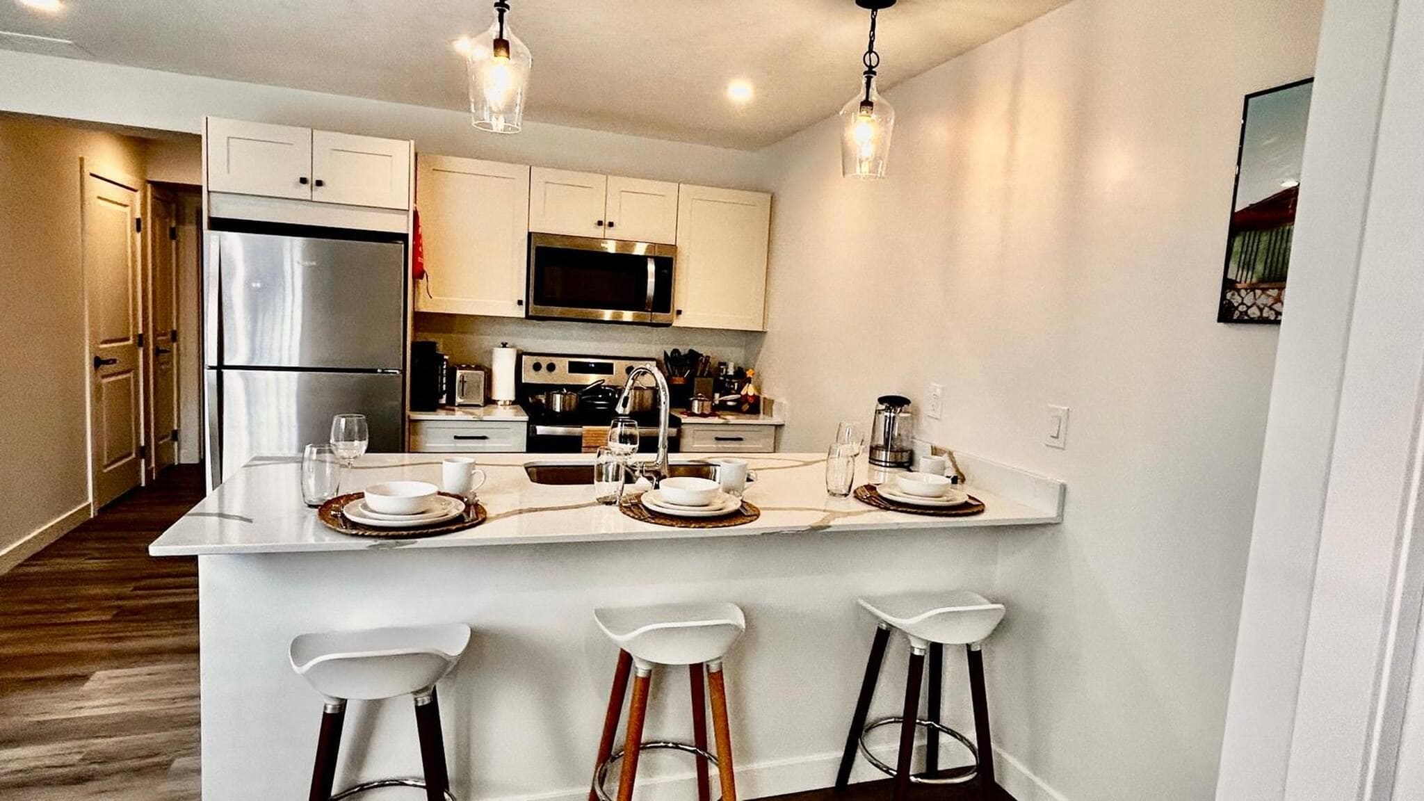 A modern kitchen with white cabinetry, stainless steel appliances, and a bar area with stools.