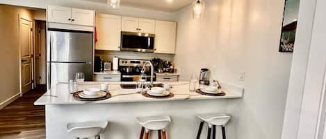A modern kitchen with white cabinetry, stainless steel appliances, and a bar area with stools.