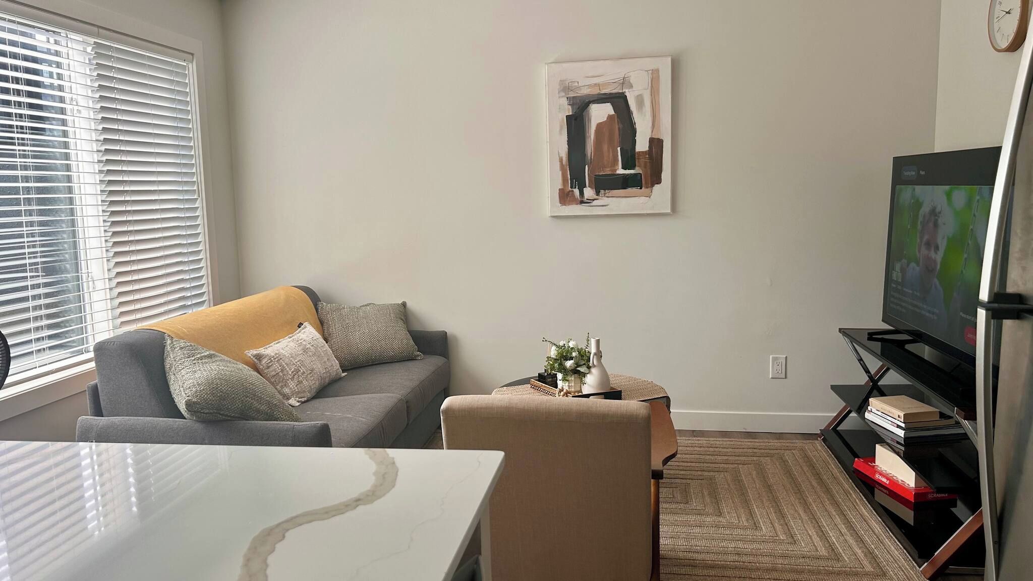A living room with a sofa, a coffee table, a television, and a painting on the wall.